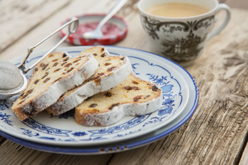 Traditional german Stollen with raisins and powdered sugar, on white and blue ceramic plate on wooden table. With espresso and jam. Traditional Christmas baking. Selective focus. Natural light