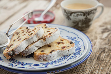 Traditional german Stollen with raisins and powdered sugar, on white and blue ceramic plate on wooden table. With espresso and jam. Traditional Christmas baking. Selective focus. Natural light