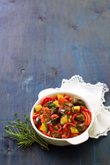 Ratatouille, a traditional French dish of vegetables in a white ceramic bowl on a dark blue background 