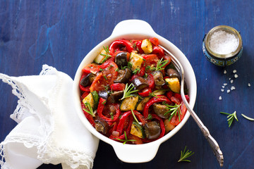Ratatouille, a traditional French dish of vegetables in a white ceramic bowl on a dark blue background 