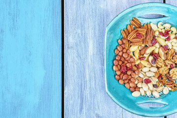 Nuts mix and cranberries on a plate, wooden surface background, top view with copy space.
