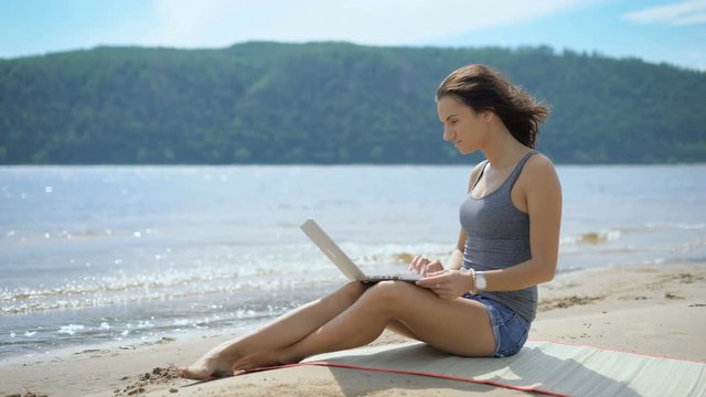 A beautiful sexy young lady is sitting at a beach using laptop