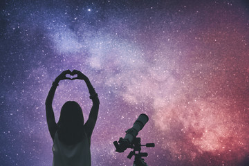 Girl making a heart-shape for the stars with telescope beside her.