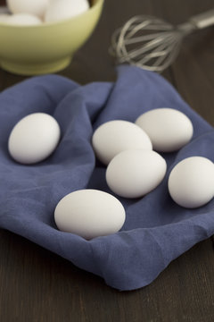 White egg on blue cloth with whisk and bowl on a wooden table.