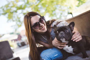 Cute teenager girl enjoying outdoors in cafe bar playing with her adorable French bulldog puppy....