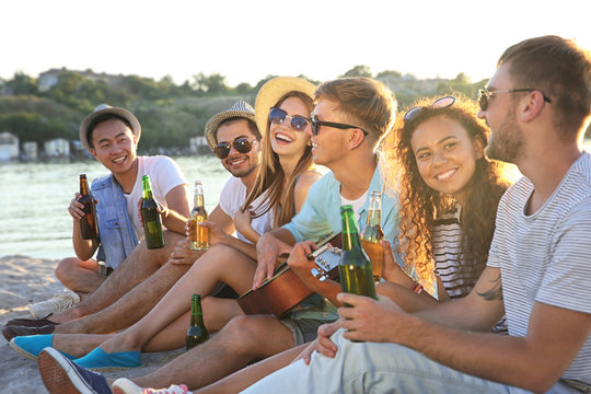 Group of friends listening to guitar and drinking beer at beach