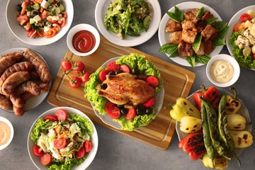 Plates with roasted chicken and different salads on table
