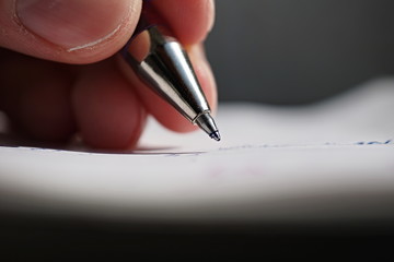 Male hand holding a sharp blue office pen and writing to the white lined notepad as a symbol of taking notes or business communication 
