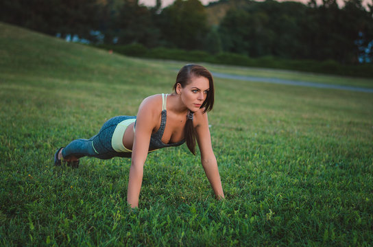 Young attractive woman training in the park. Exercise plank. Fit