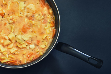 Cooked vegan green beans stew in black pan on dark background. Top view with copy space