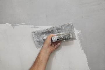 Worker spreading plaster to wall, closeup of hand and trowel tool