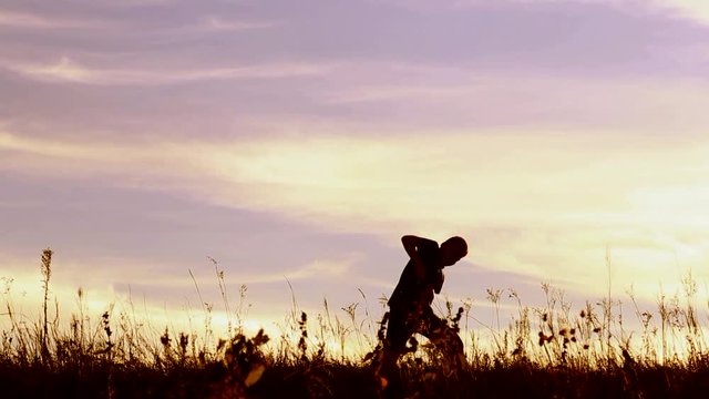 Silly dance of funny child outdoors over golden twilight sky. 9 years old boy dancing alone in beautiful nature  landscape. Silhouette of kid at sunset sky background. Real time full hd video footage.