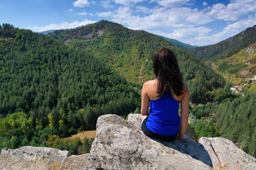 Naklejka premium A girl is sitting on the edge of a cliff and looking at a mountain