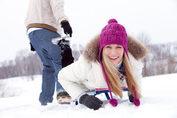 Young woman lying on sled behind her boyfriend