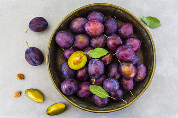 Ripe plums in a old bowl on a gray stone background.