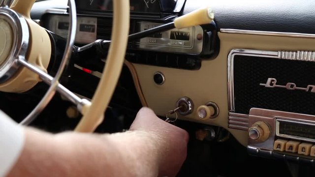 The driver starts the engine of a vintage car, he turns the key in the ignition
