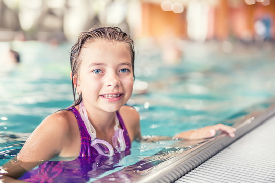 Portrait of a cute young girl with goggles in swimming pool. Swimming training.