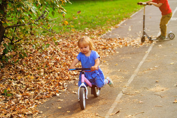 little girl on runbike and boy at scooter in autumn, kids sport