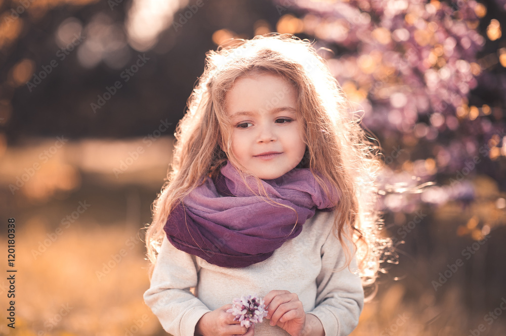 Wall mural cute baby girl 3-4 year old holding flower wearing stylish clothes outdoors.