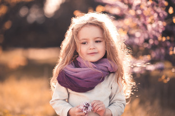Cute baby girl 3-4 year old holding flower wearing stylish clothes outdoors.