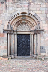 The entrance door of dark textured metal, in Viborg Cathedral, build of ashlar granite, sandstone and red stone from the island Fur