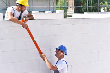 Zusammenarbeit auf der Baustelle - Handwerker/ Maurer errichten ein Haus // Cooperation on the...