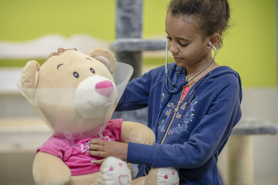 Naklejki Girl playing veterinarian with teddy bear