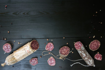 Pieces and slices of salami with mold, pepper on dark wooden bac
