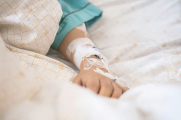 Closeup saline water line at the hand of patient on bed in hospital room