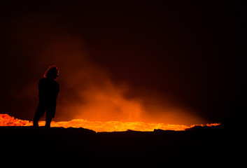 Fototapeta premium Person standing at the edge of Erta Ale active volcano at night
