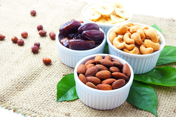 Close up of mixed nuts with roasted almonds, cashew nuts, date fruits and dried banana in a bowl on a sackcloth background. Selective focus.