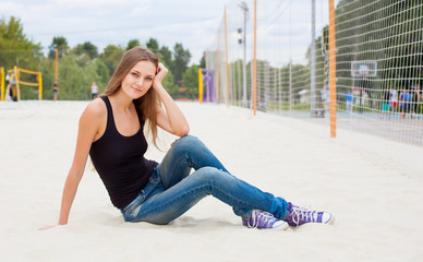 Beautiful young girl sitting on the sand nex to the net for volleyball of Sunny warm day