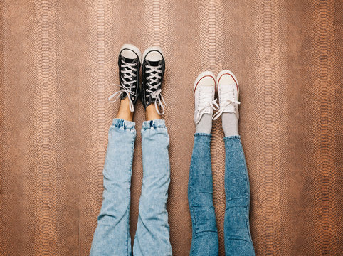 Young Fashion Couple's Legs In Jeans And Sneakers Feet Up On The Wall. Indoor. Warm Color