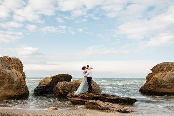 Wedding. Wedding by the sea. Young couple in love, bearded groom and bride in wedding dress at the seaside. Couple in love walking around the sea and the rocks near the place of the wedding ceremony