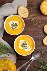 Pumpkin cream soup with cream and pumpkin seeds on wooden background, top view