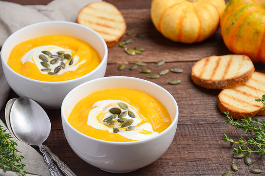 Pumpkin cream soup with cream and pumpkin seeds on wooden background, selective focus