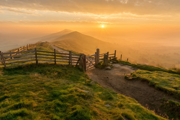 Naklejka premium Golden sunrise at Mam Tor in the English Peak District on a hazy Autumn Morning with wooden gate.