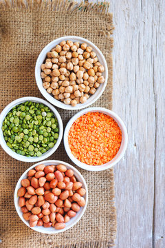 Top view of health benefits of dried peanuts, chick peas,  red lentils and green peas on a wooden table.