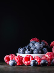 Mix of raspberry and blueberry on dark background, black wooden