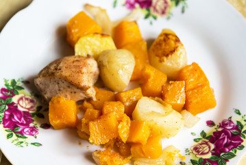 Chicken baked with slices of potato and a pumpkin on the plate