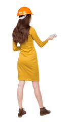 Backview of business woman in construction helmet stands and enjoys tablet or using a mobile phone. Standing young girl. Rear view people collection.  backside view of person.  Isolated over white
