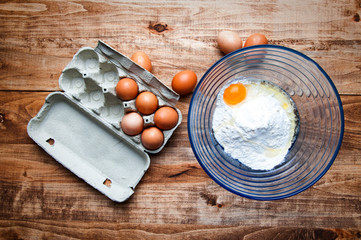 The image of eggs and flour on a wooden table.
