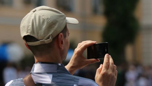 Male passer-by filming accident site on phone, defocused crowd of bystanders