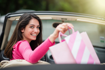 Cheerful woman in her convertible car depositing shopping bags