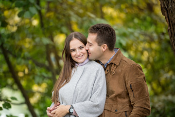 Fototapeta premium Romantic couple relaxing in autumn park, cuddling, kissing, enjoying fresh air, beautiful nature, nice fall weather. Beloved spending time together. Yellow leaves in background