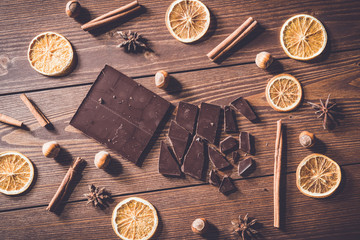 Dark chocolate bars with dry orange slices, cinnamon sticks and hazelnuts on wooden table