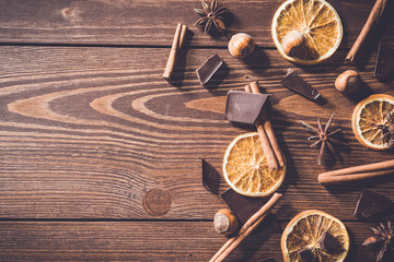 Dark chocolate bars with dry orange slices, cinnamon sticks and hazelnuts on wooden table