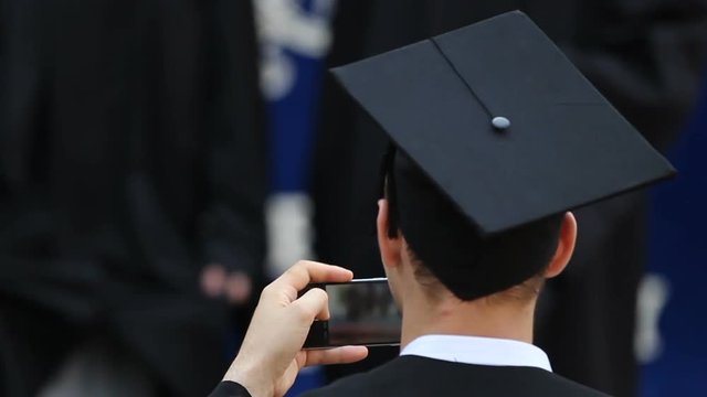 Young man taking picture of happy university graduates on phone, youth memories