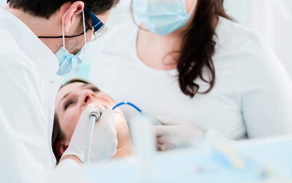 Dentist treating woman patient with drill