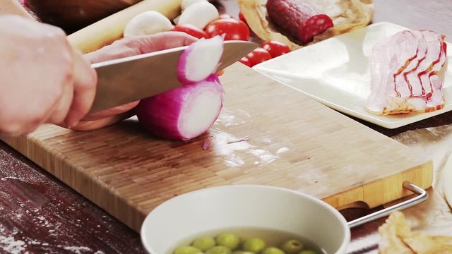 Mens hands cut onion on bamboo cutting board for cooking pizza. Pizza ingredients on wooden background
